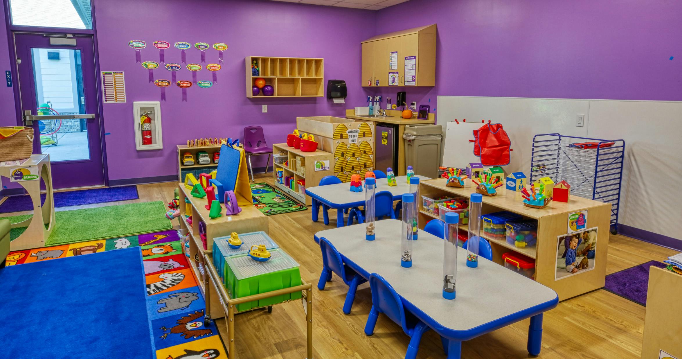 A colorful classroom with purple walls, small tables, chairs, and toys