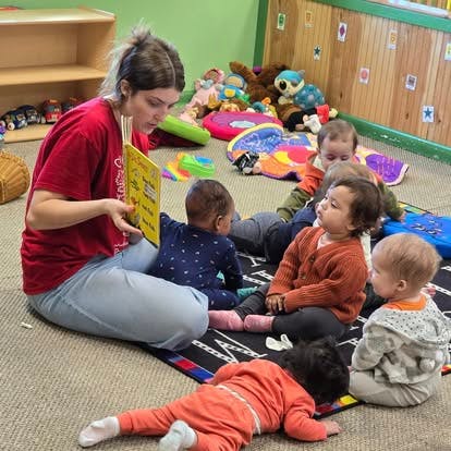 A person reading a book to a group of children in a childcare setting