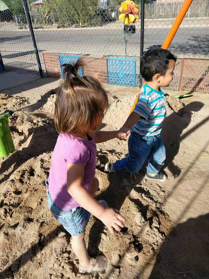 Two children holding hands in a sandbox
