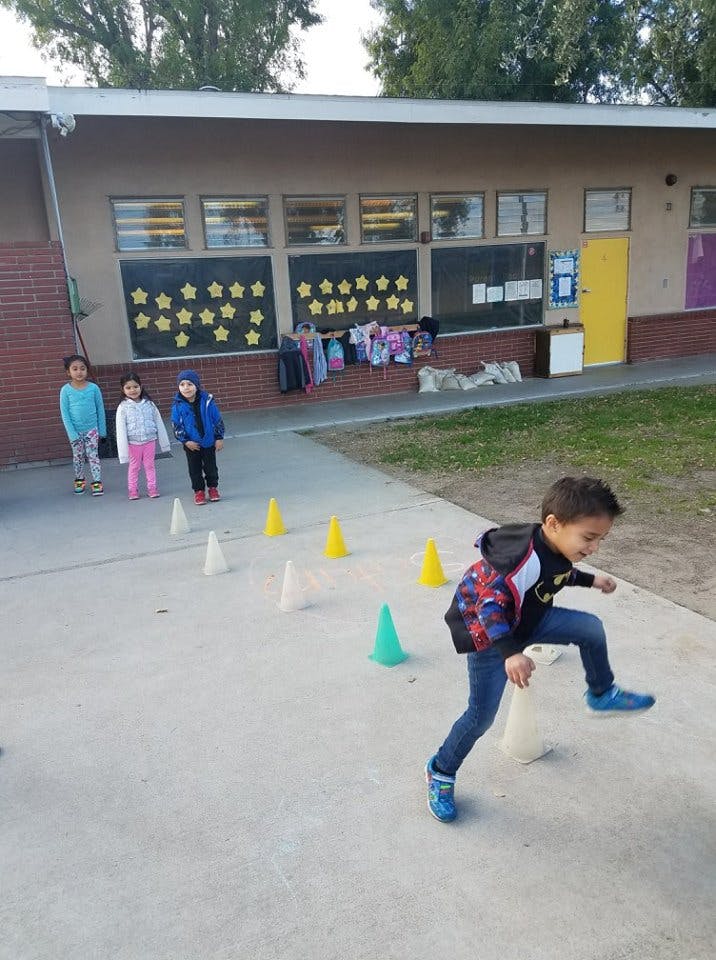 Child stepping over a cone with other children standing in the background