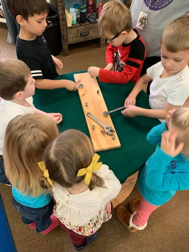 Children gathered around a table, playing with a wooden board with nuts and bolts