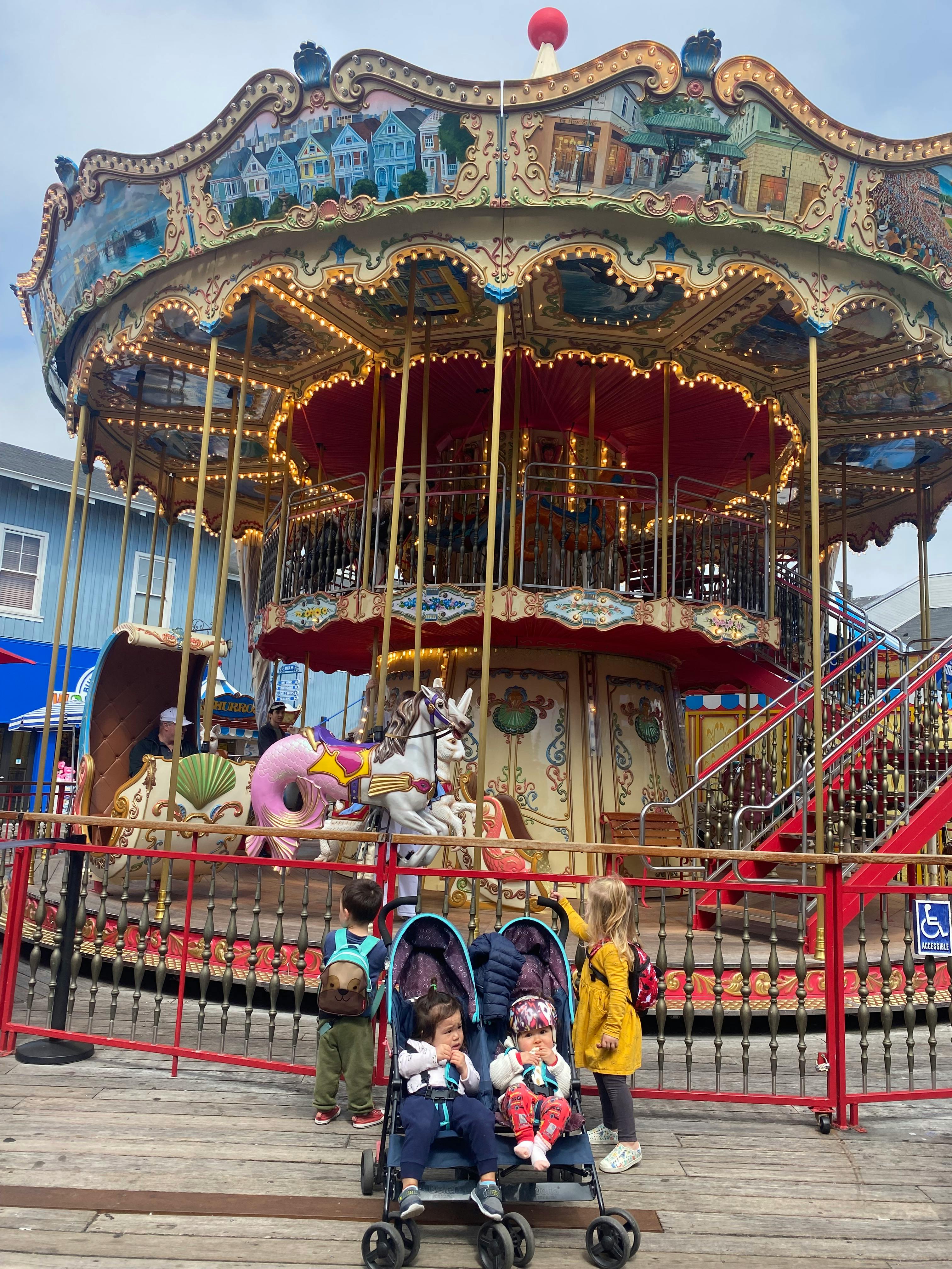 Children and babies in strollers in front of a carousel