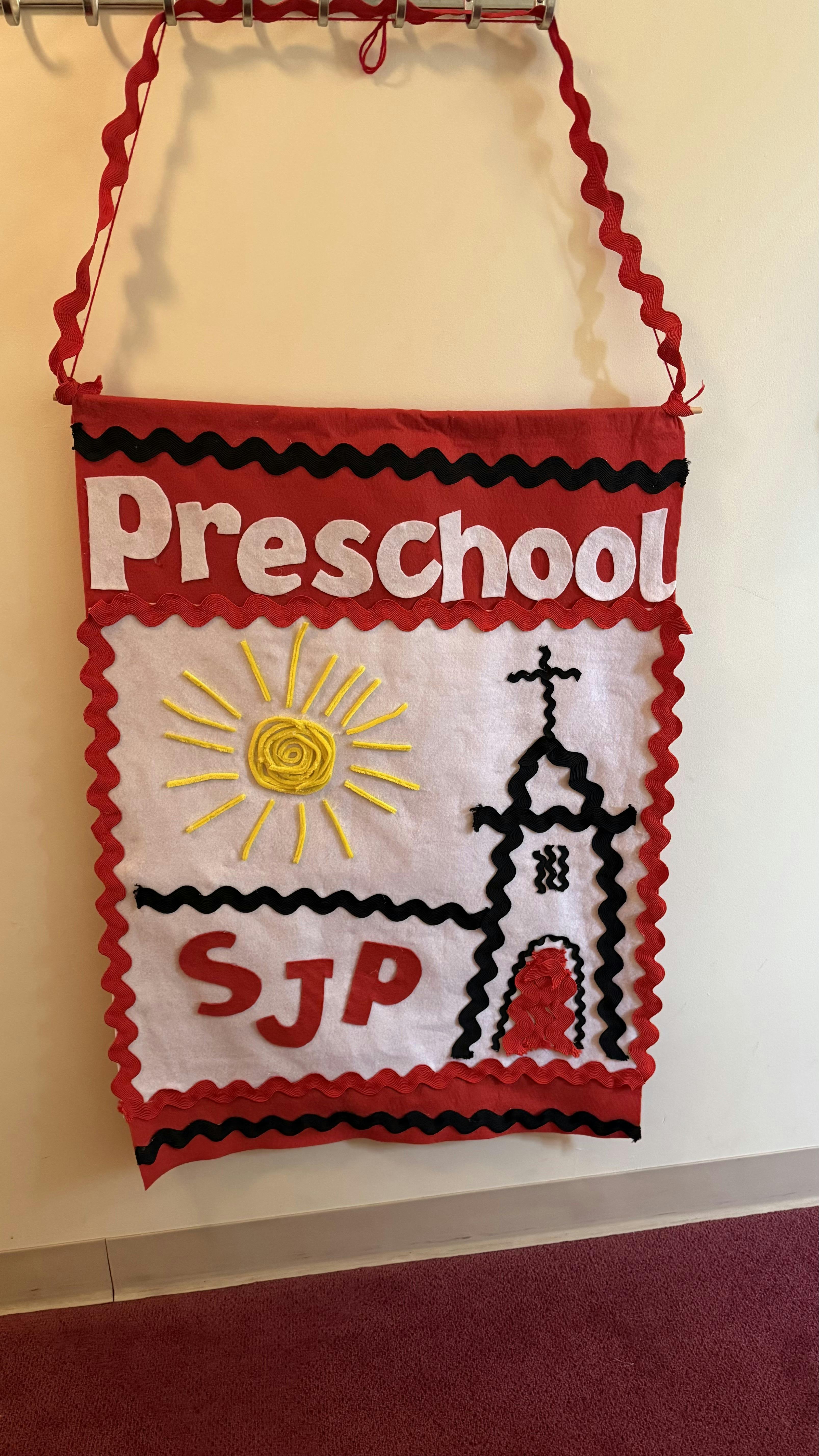 Red and white banner with "Preschool" and "SJP" text, sun, and church