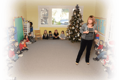 Person standing in a classroom with children sitting on the floor