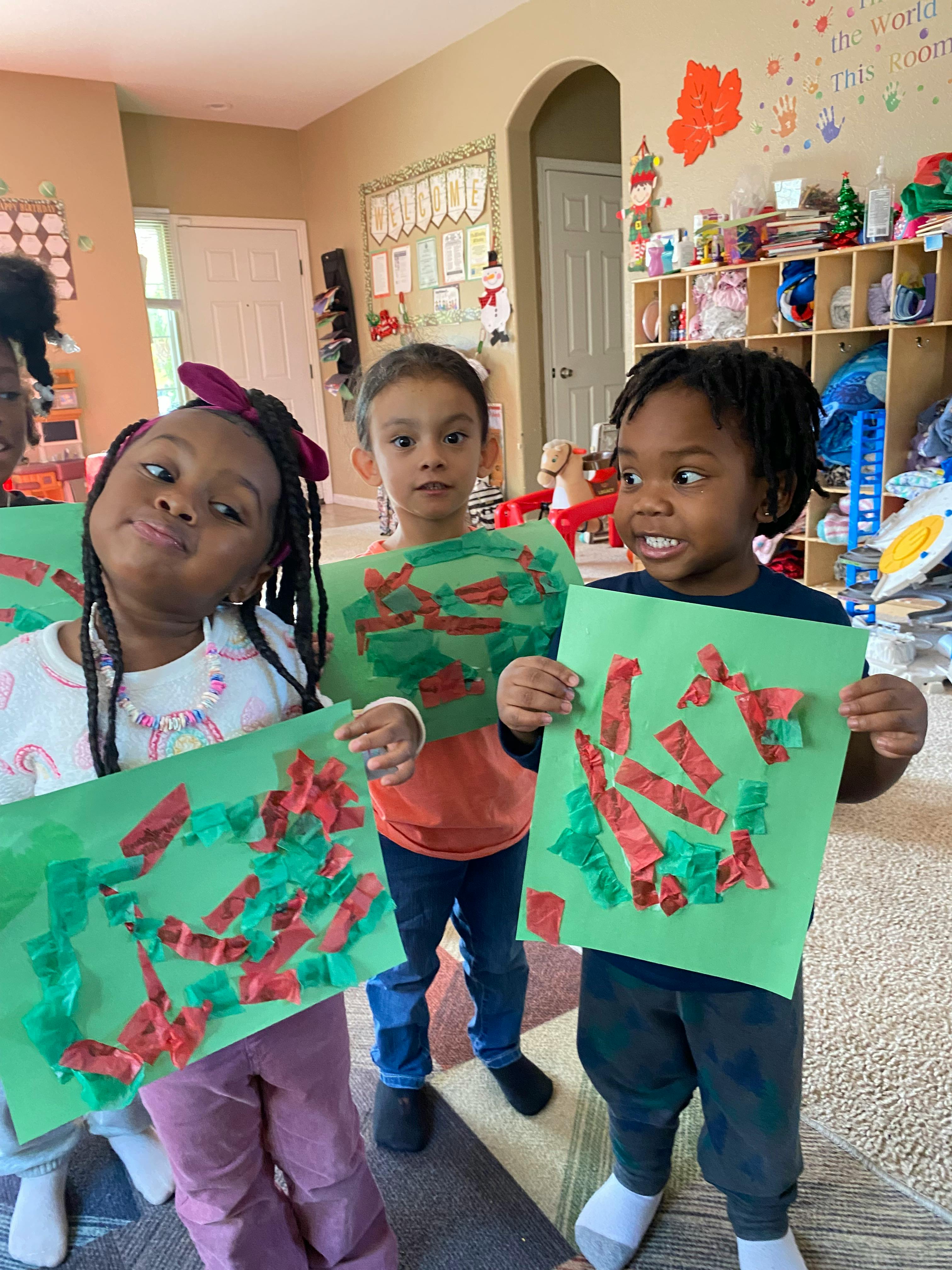 Three children holding up green papers with red and green tissue paper glued on them