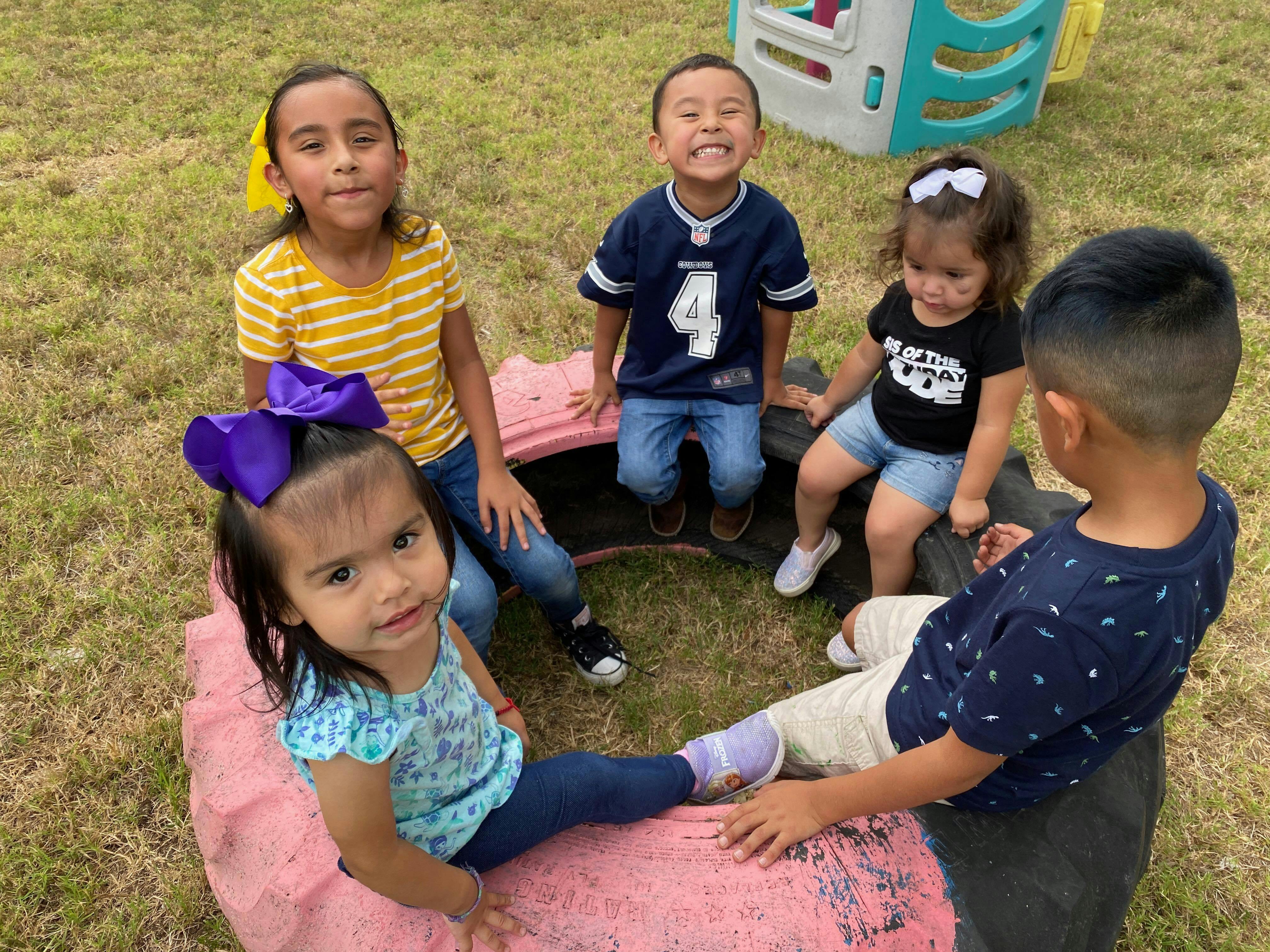 Five children sitting on tires on grass