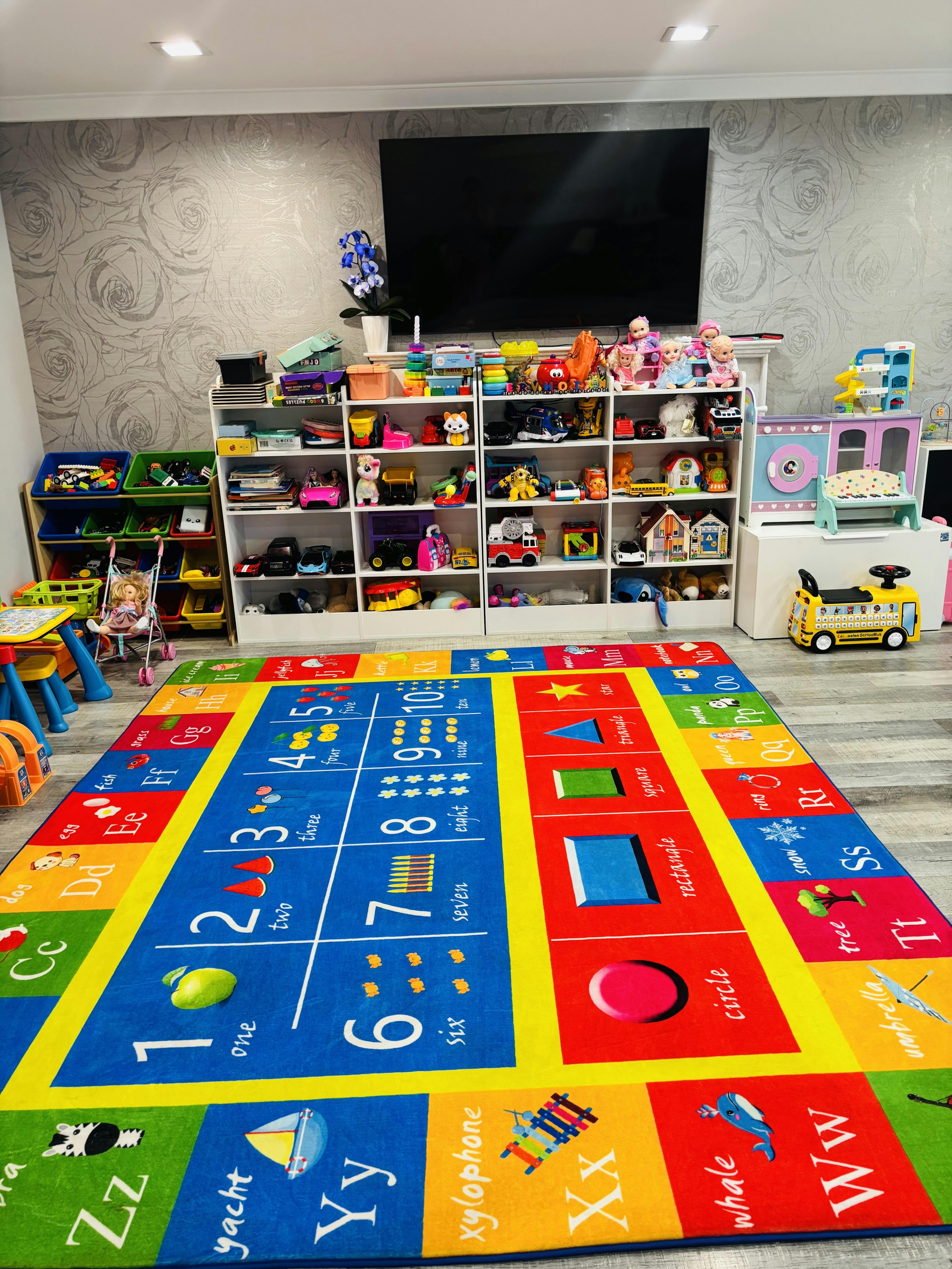 Children's playroom with a colorful educational rug, toy shelves, and a TV