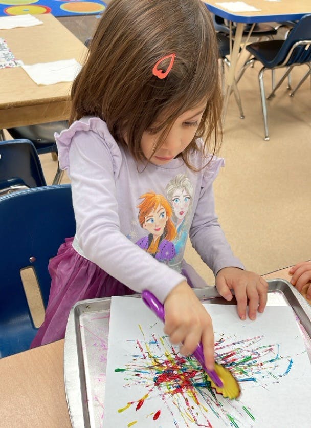 Child painting with a brush on paper in a classroom