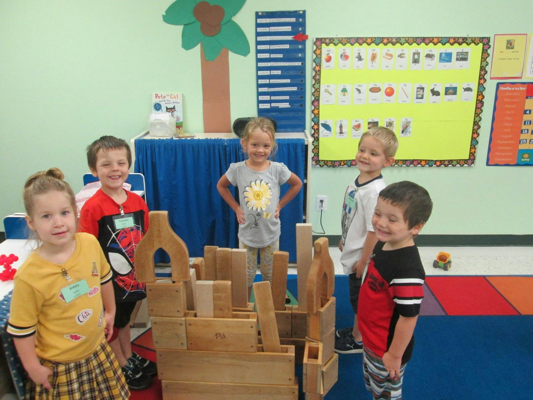 Five children standing around wooden blocks in a classroom
