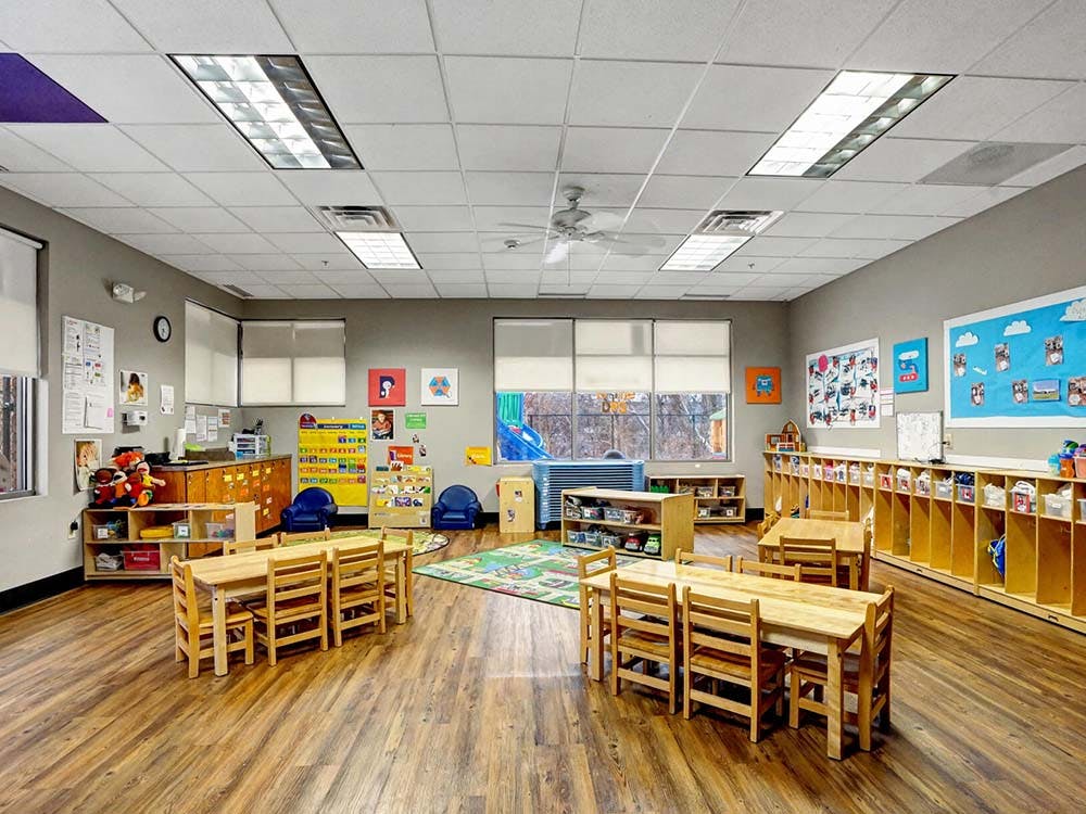 Empty classroom with small wooden tables and chairs, shelves, and colorful decorations