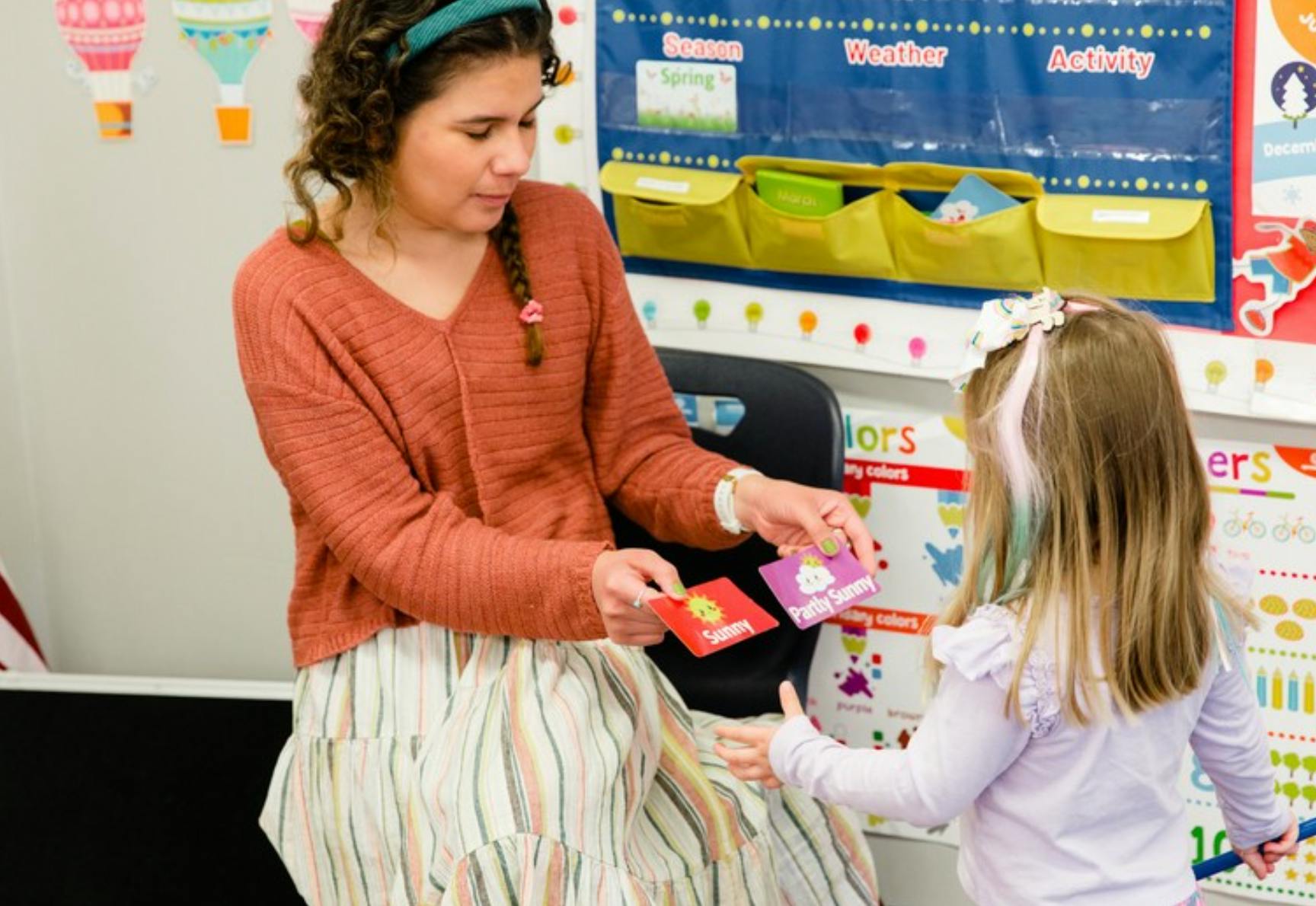 Person holding weather cards for a child in a classroom