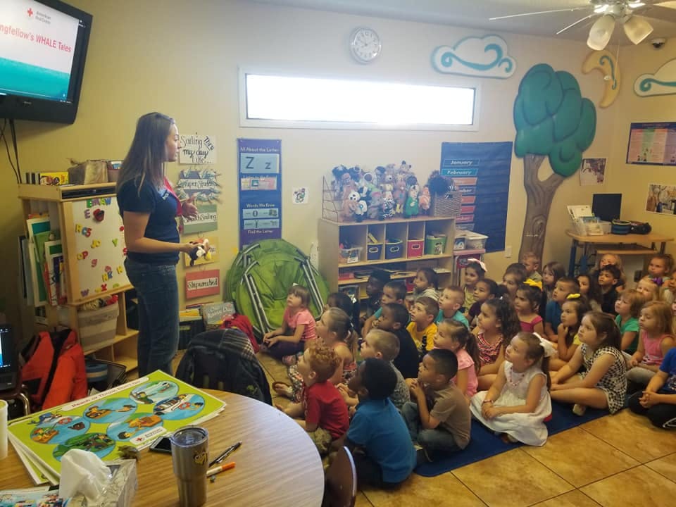 Person speaking to a group of children sitting on the floor in a classroom