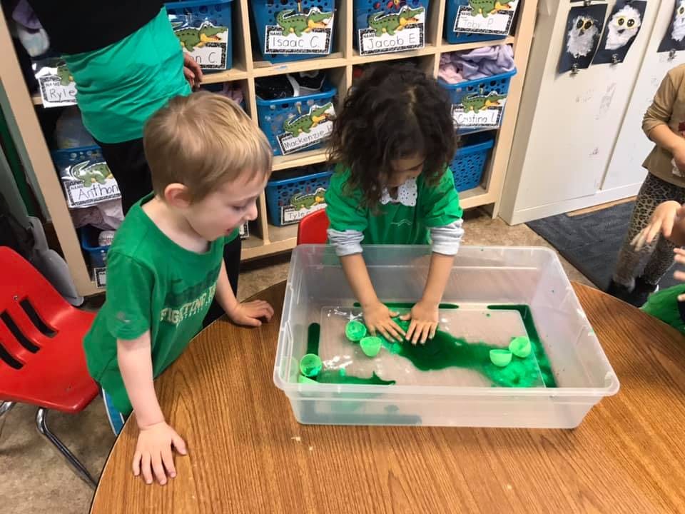 Child playing with green liquid and objects in a clear bin, plastic bin