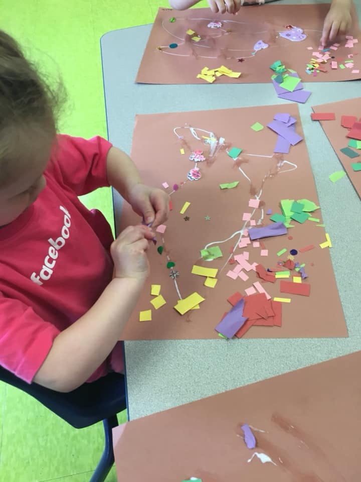 Child making art with paper cutouts and string
