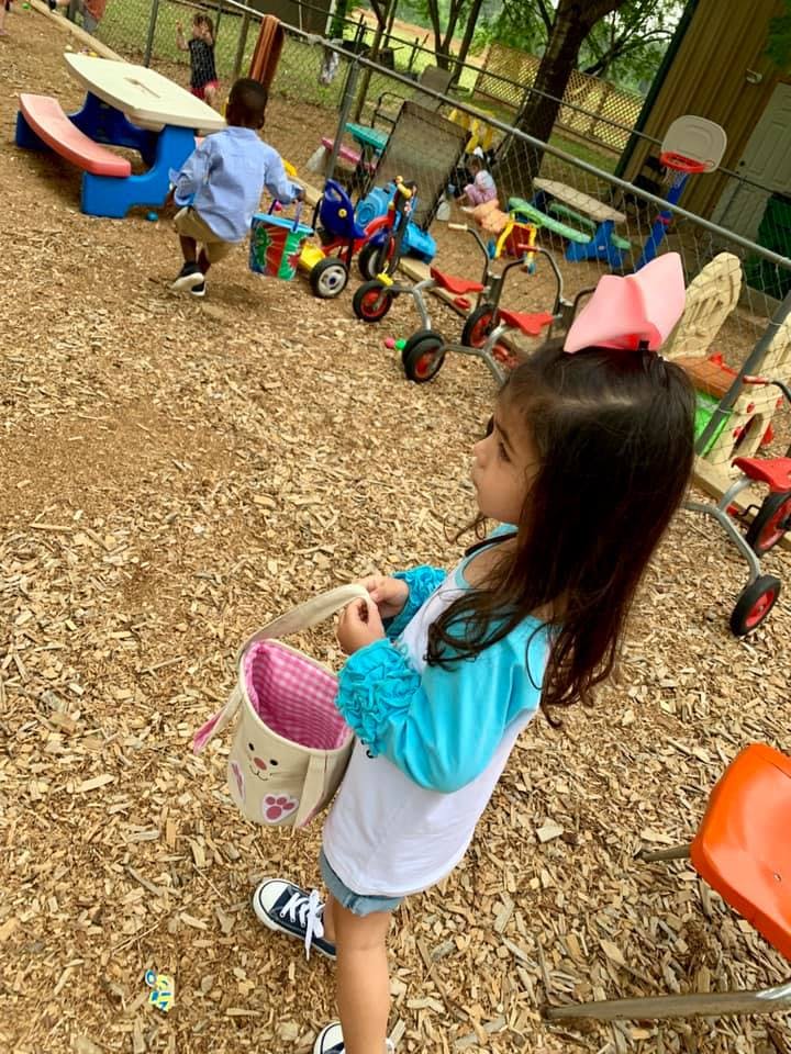 Child holding a basket on a playground with other children and toys