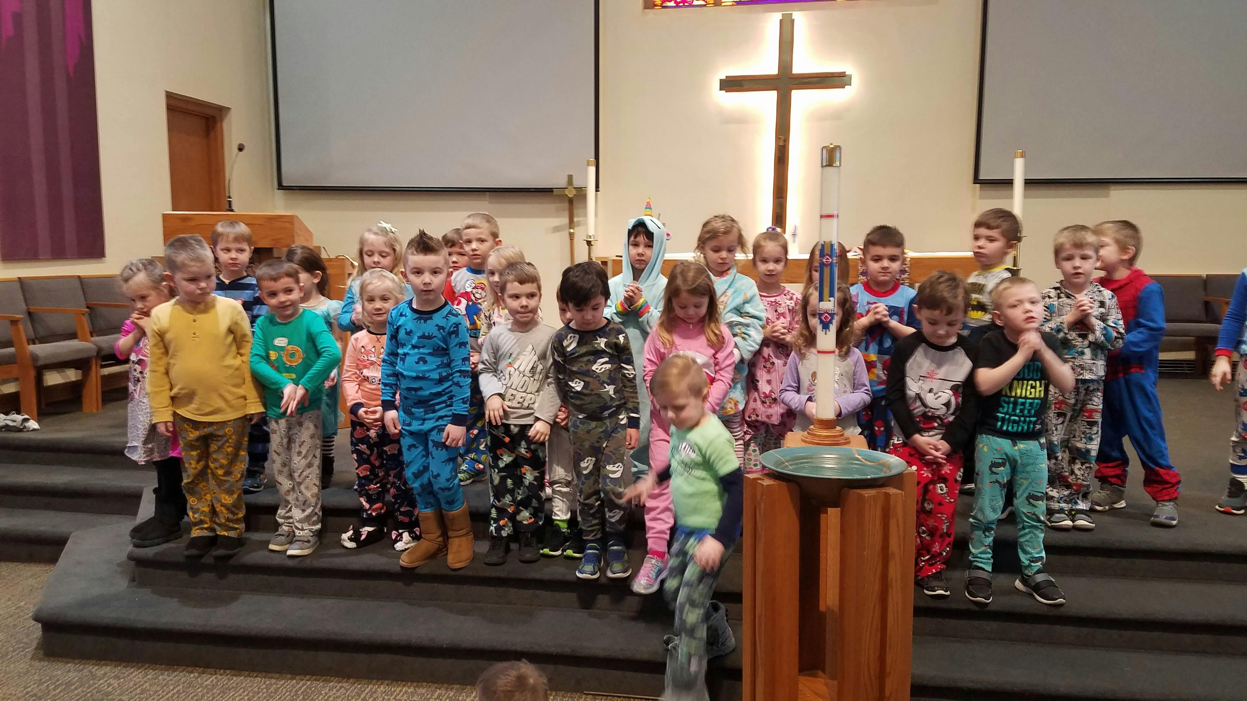 Group of children in pajamas standing on steps in front of a cross