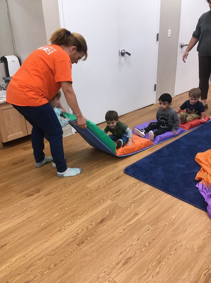 Adult holding a mat with a child on it, other children sitting on mats