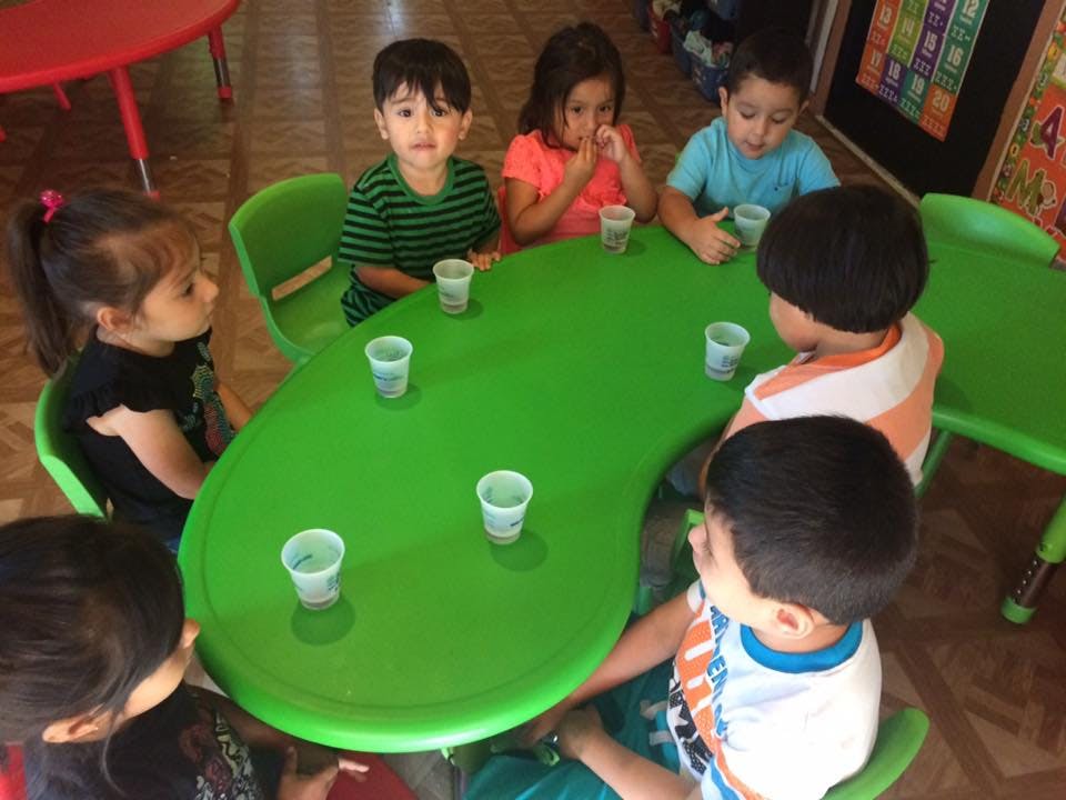 Children sitting around a green table with small cups