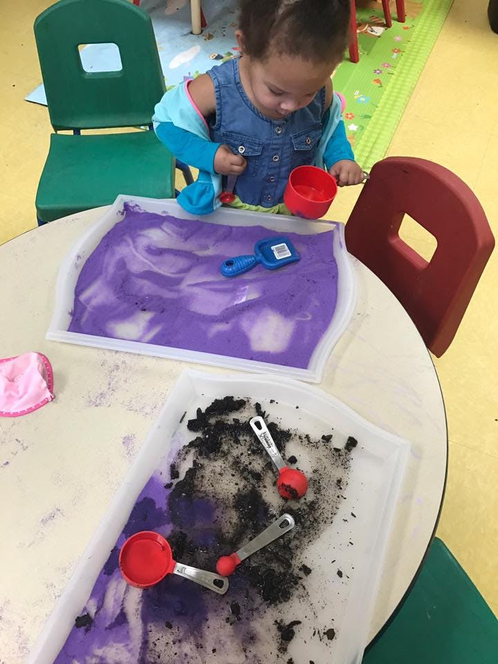 Child playing with purple sensory material and measuring spoons at a table