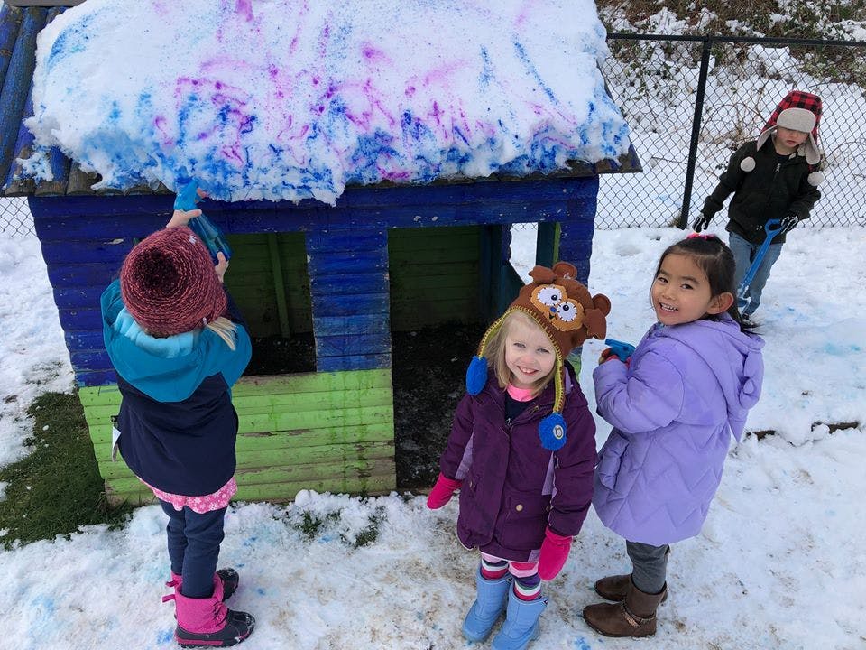 Children playing in snow around a small playhouse