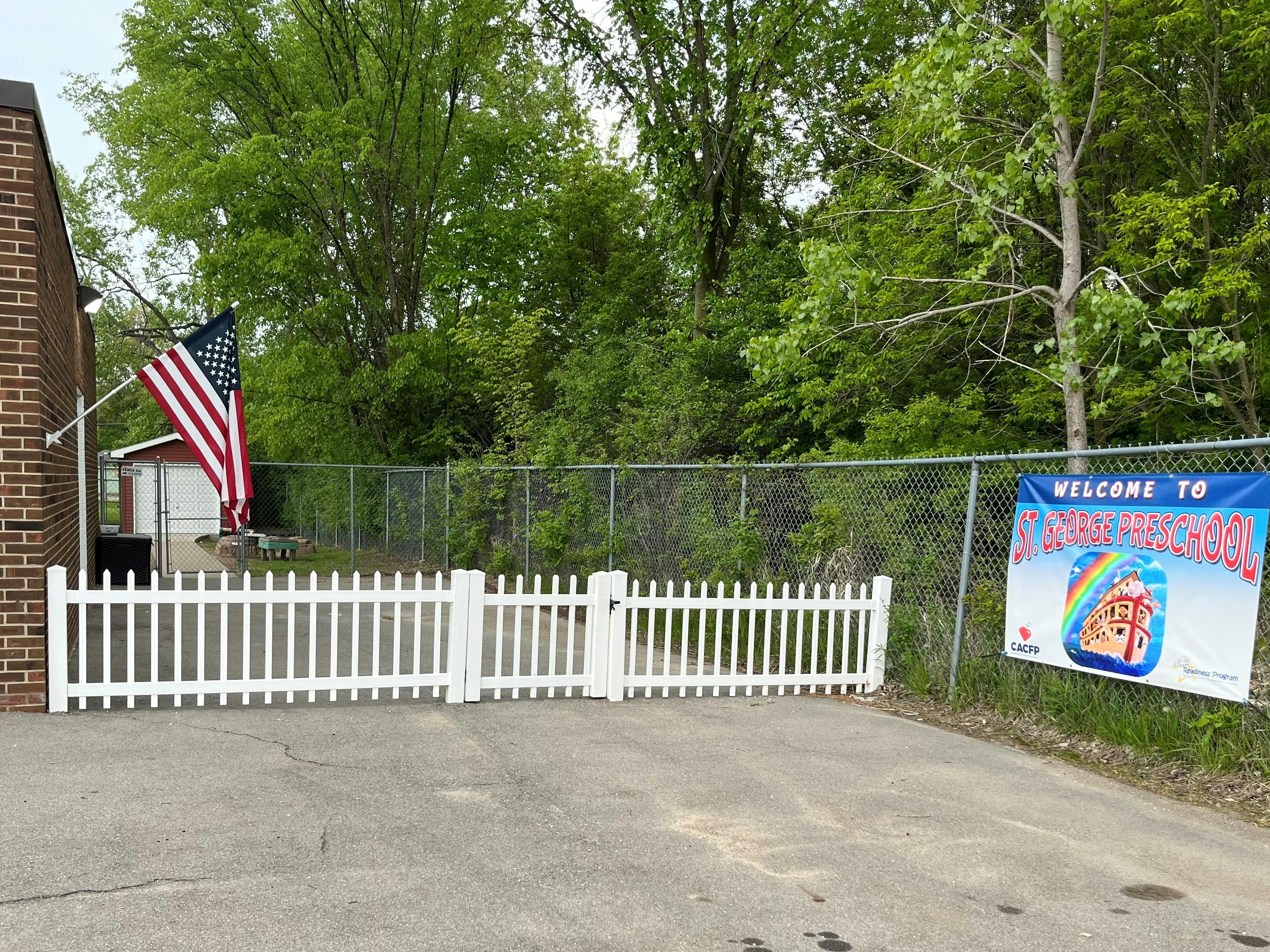 American flag on a brick building next to a white picket fence and chain link fence