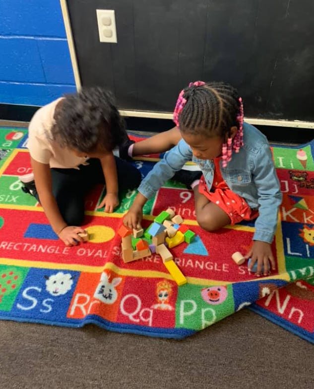 Two children playing with colorful blocks on an alphabet rug