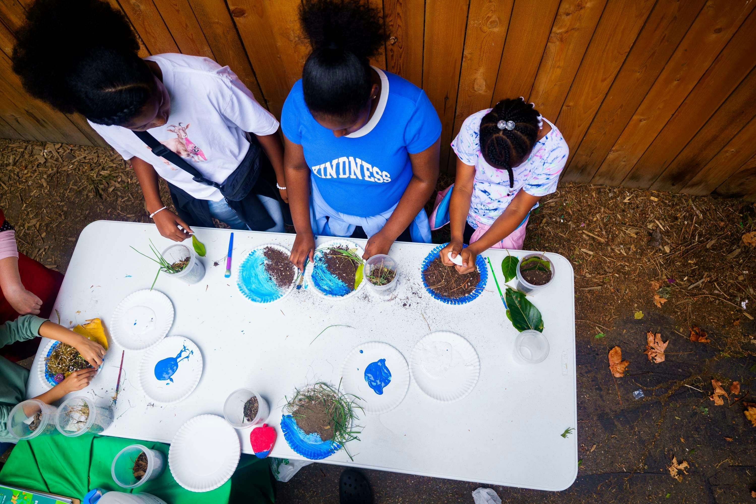 People doing an outdoor activity with paint, dirt, and plants on a table