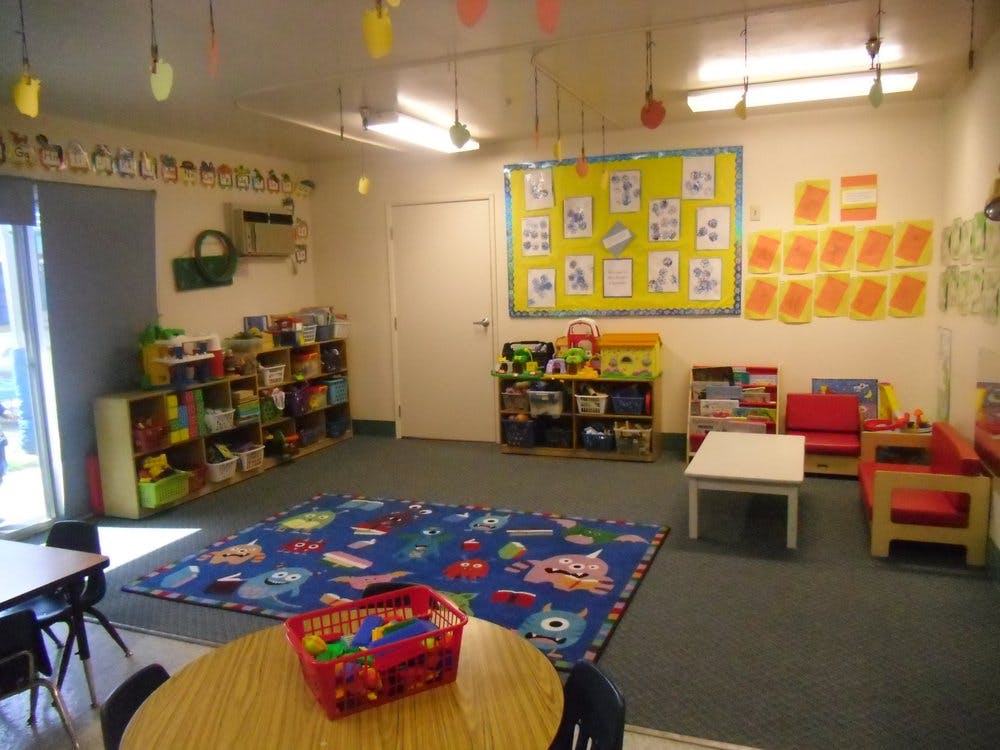 Classroom with a blue rug, shelves of toys, and small tables and chairs