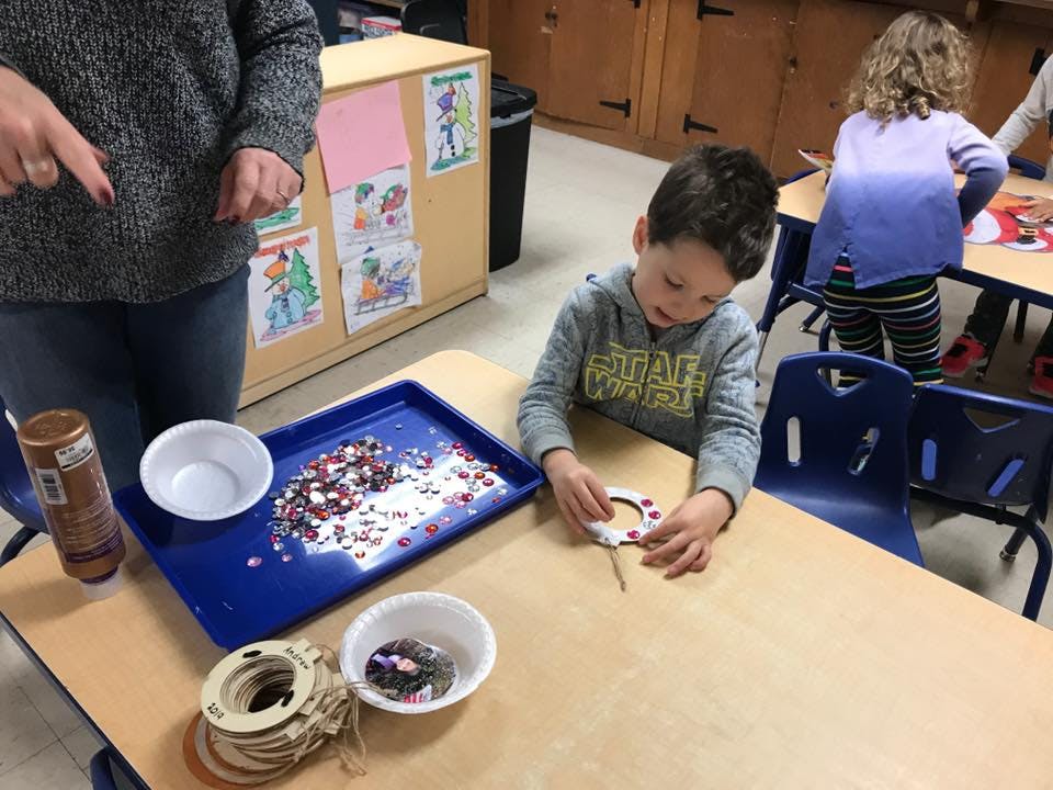 Child making a craft at a table with an adult nearby