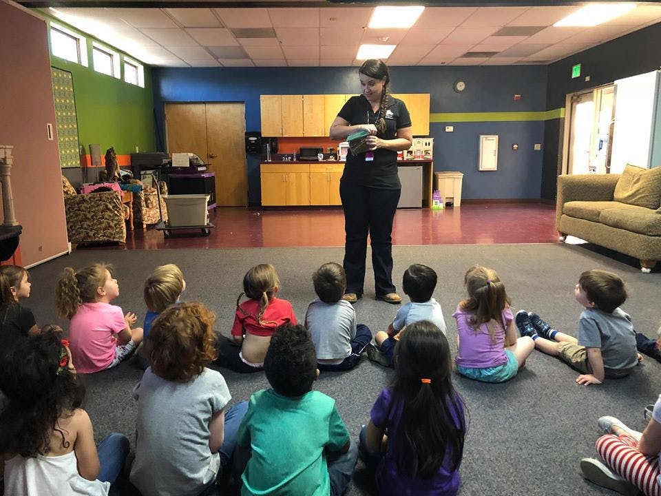 Person standing and speaking to a group of children sitting on the floor