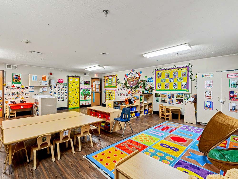 Colorful classroom with child-sized tables and chairs, and a play rug
