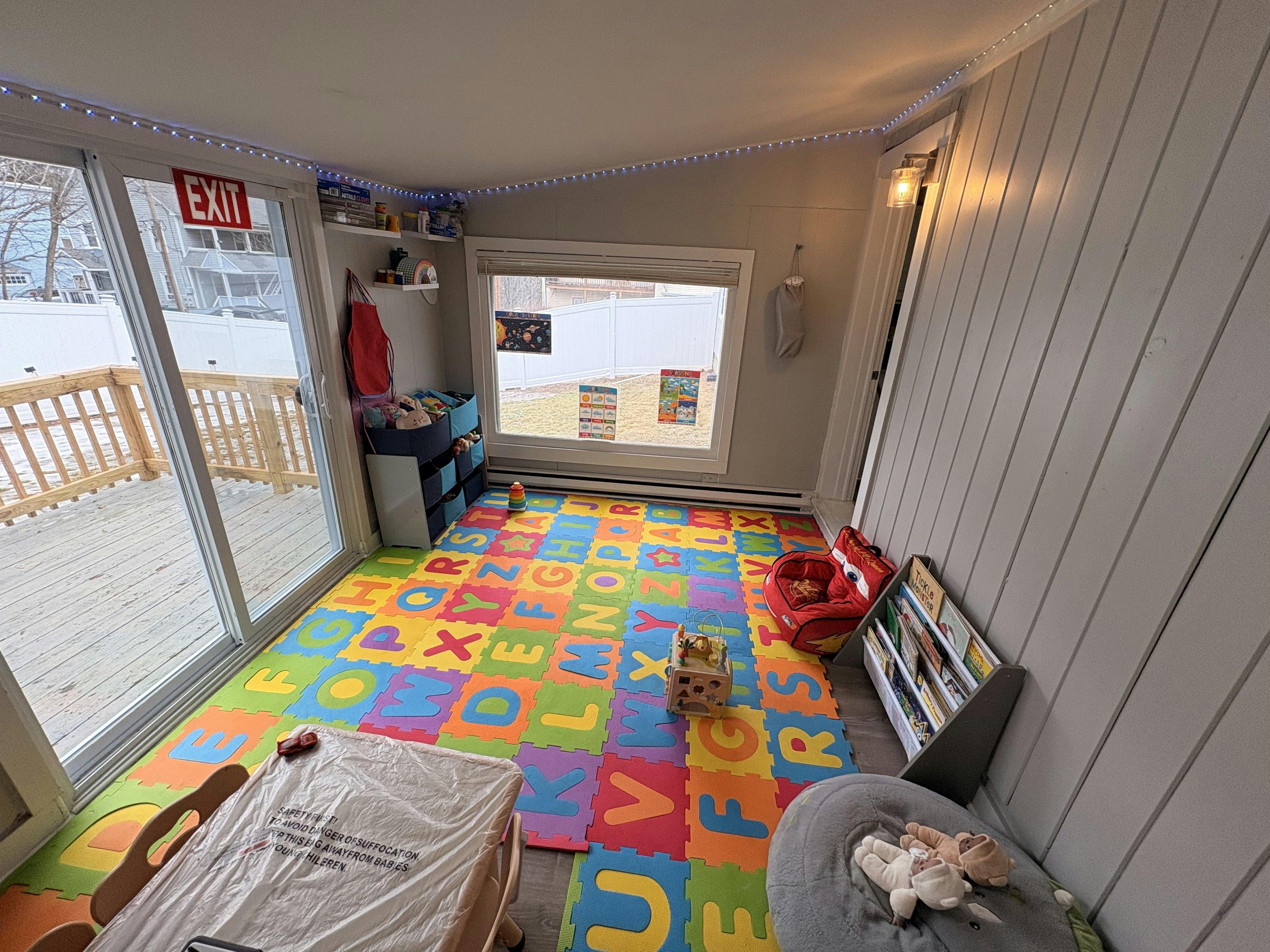 Playroom with a colorful alphabet floor mat, toys, and a window overlooking a yard