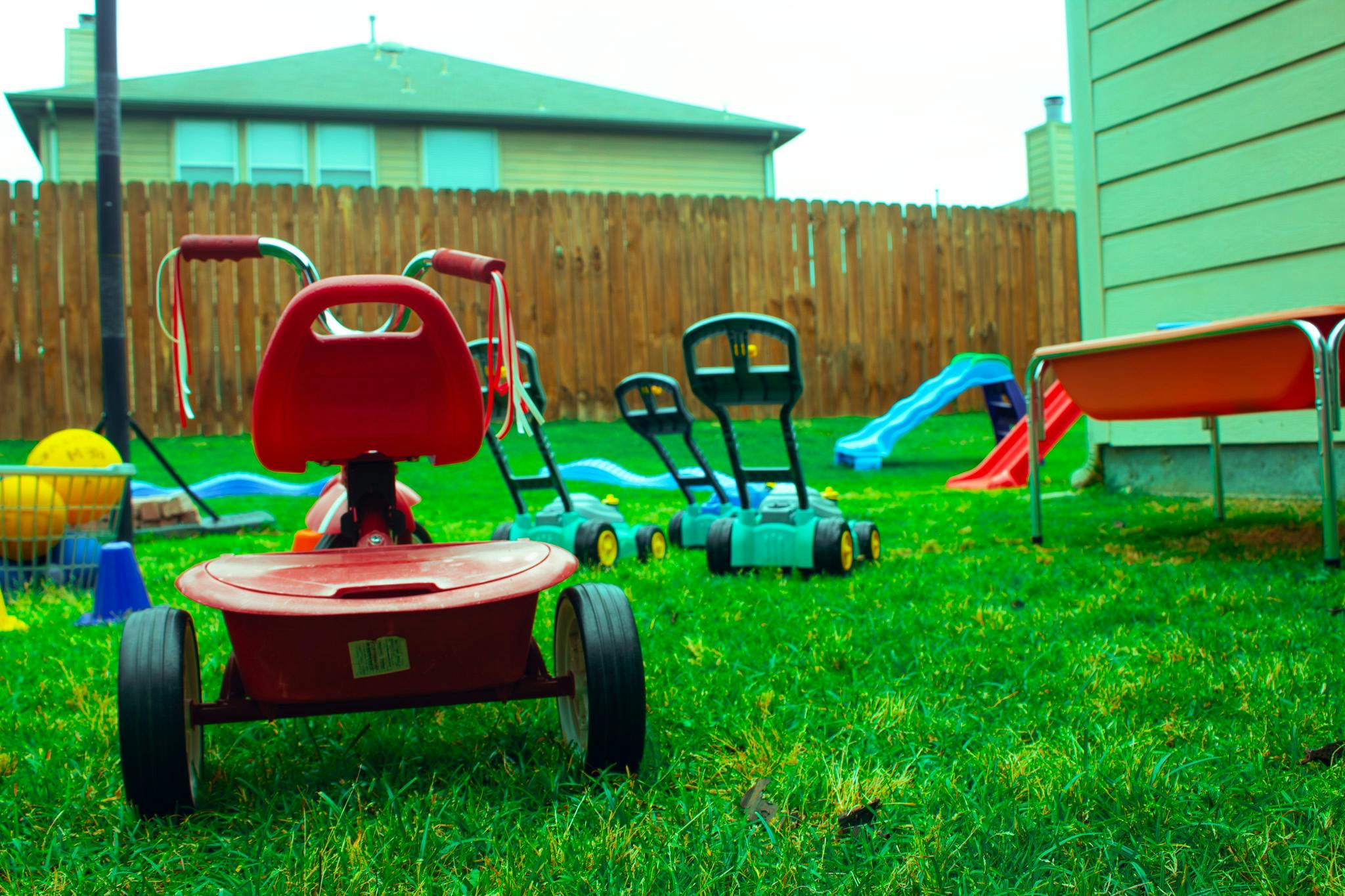 Red tricycle on grass with toy lawnmowers and slides in a backyard