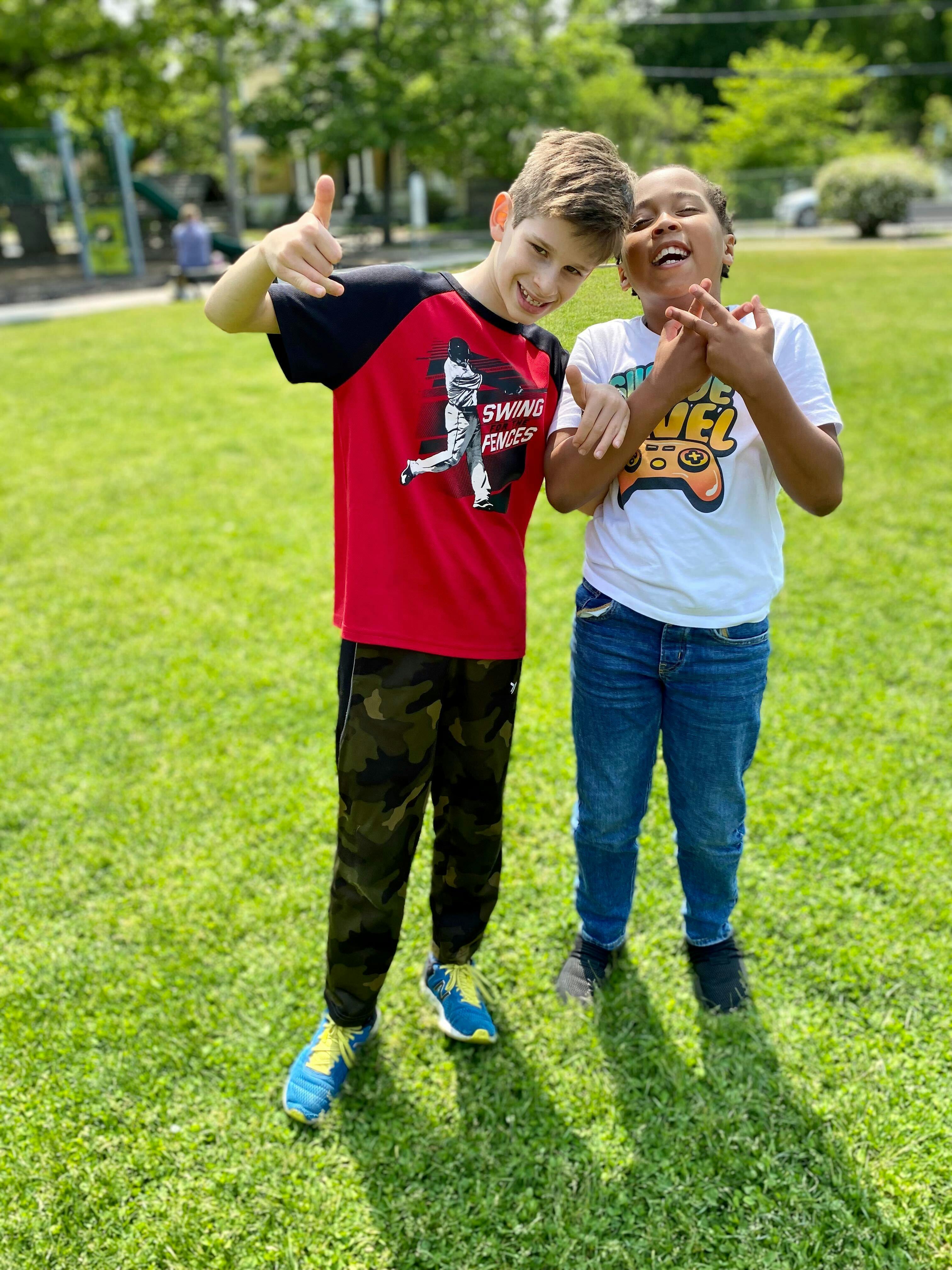 Two children standing on grass, one giving a thumbs up