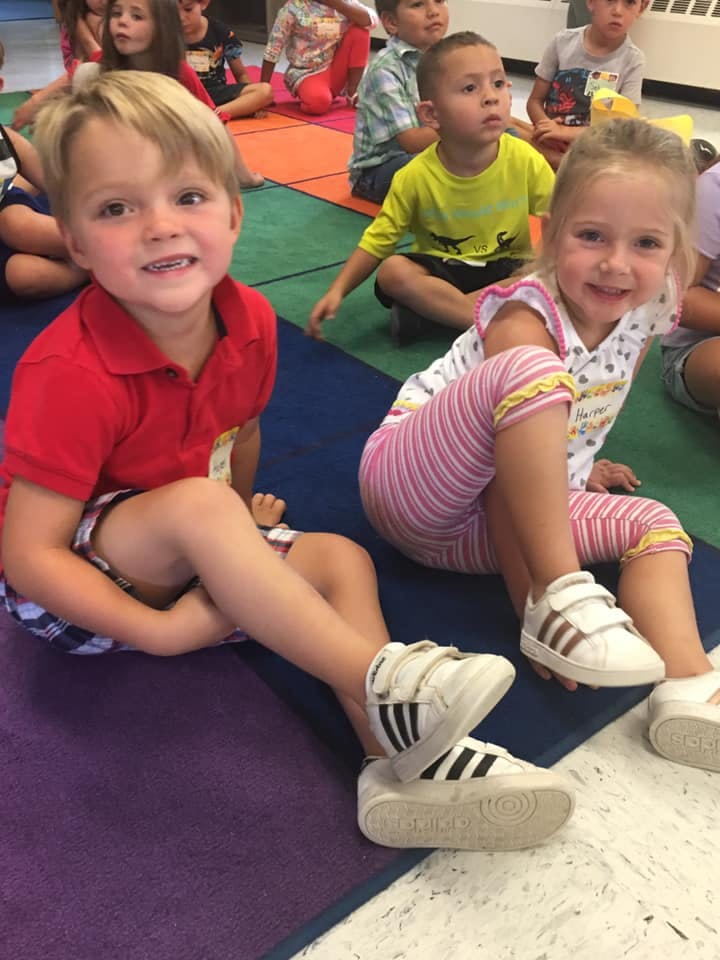 Two children sitting on a colorful mat in a classroom