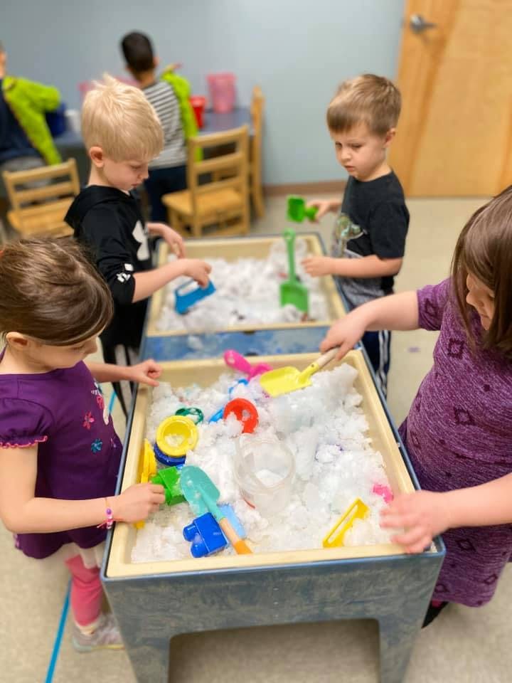 Children playing at a sensory table with white material and colorful toys
