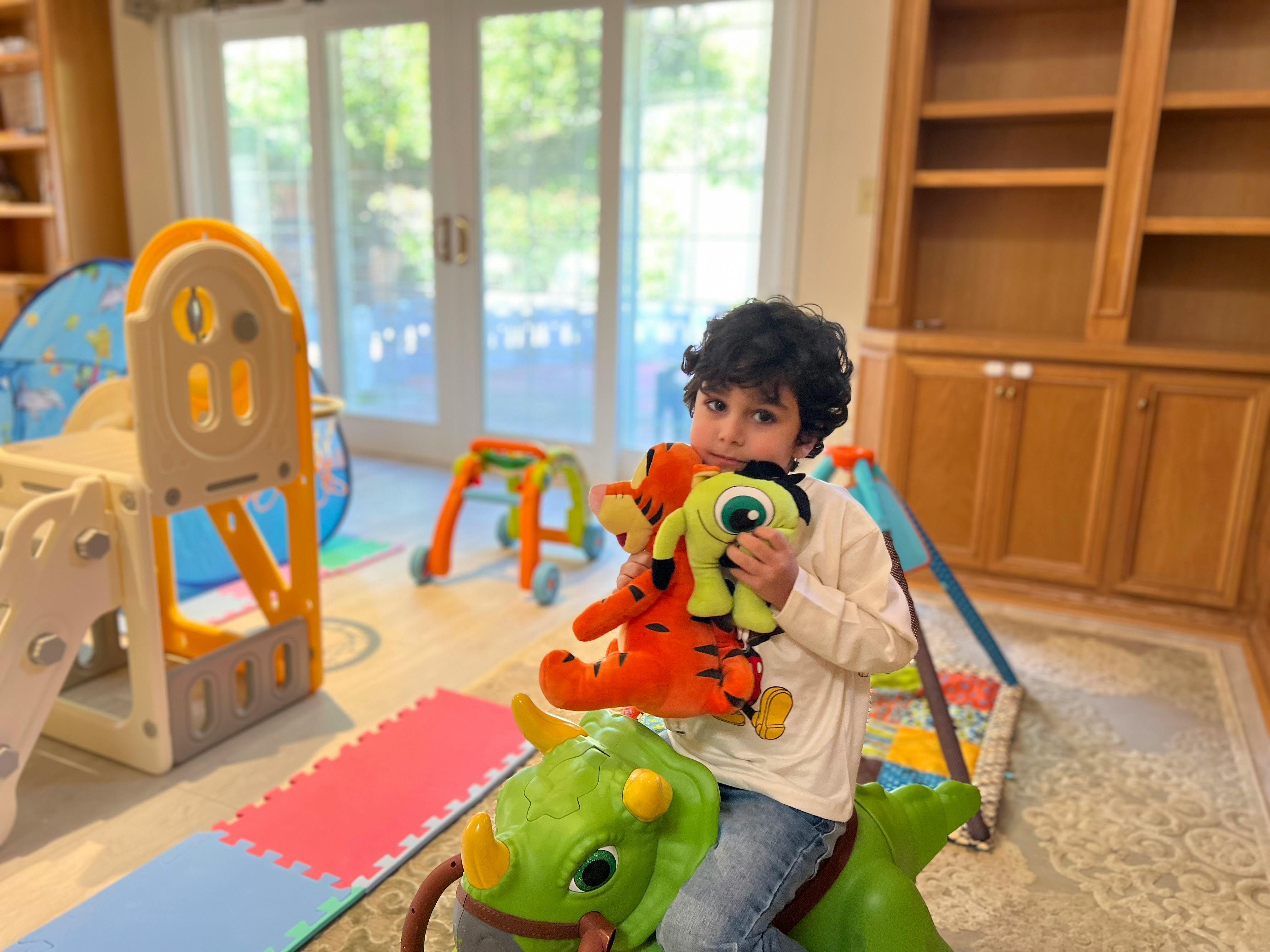 Child holding two stuffed animals while sitting on a toy