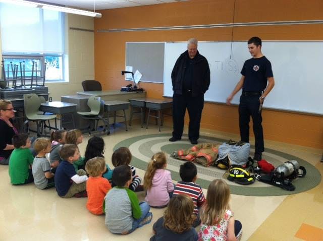 Two people presenting to children sitting on a rug in a classroom