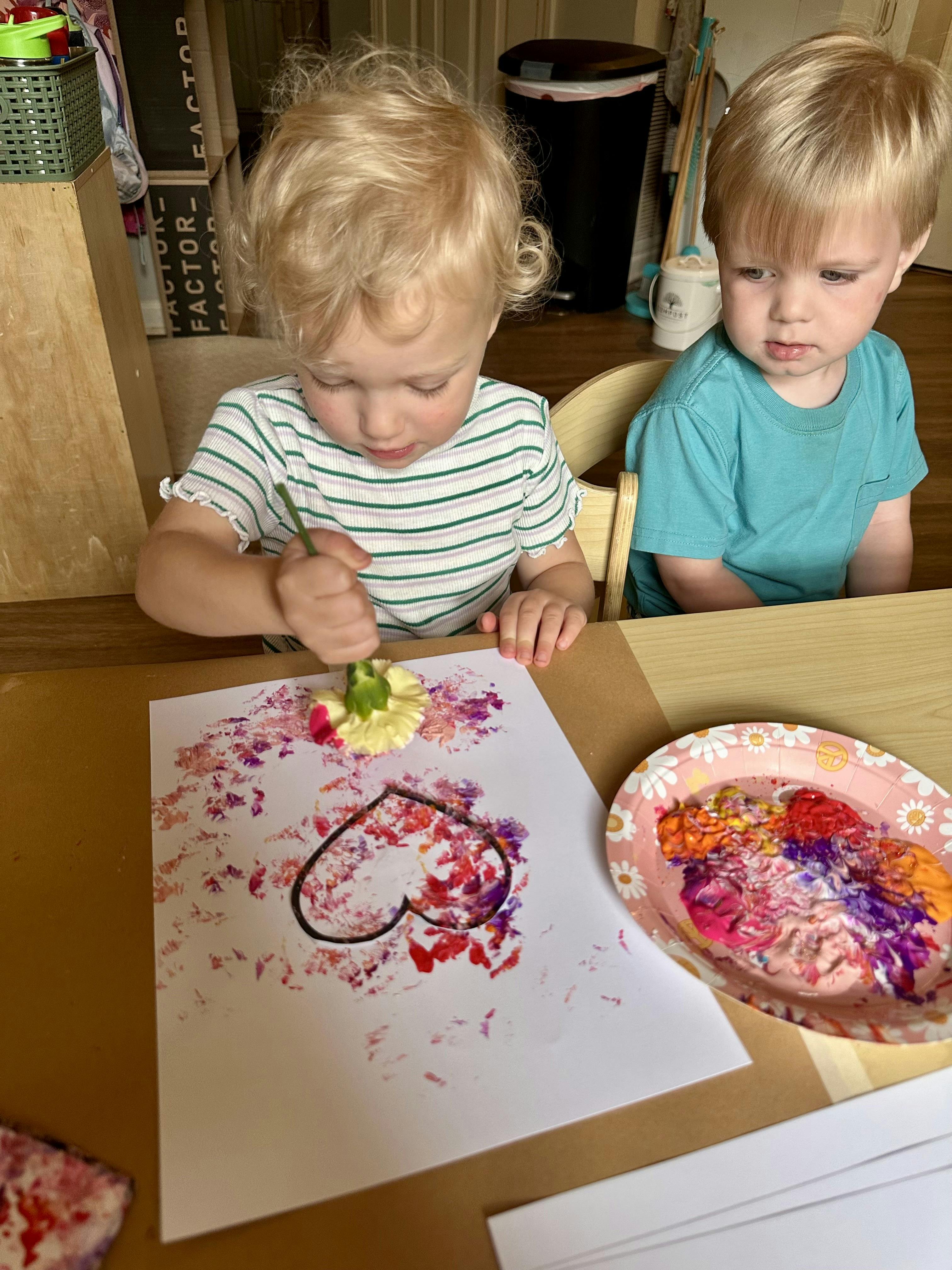 Child painting a heart on paper using a flower as a brush