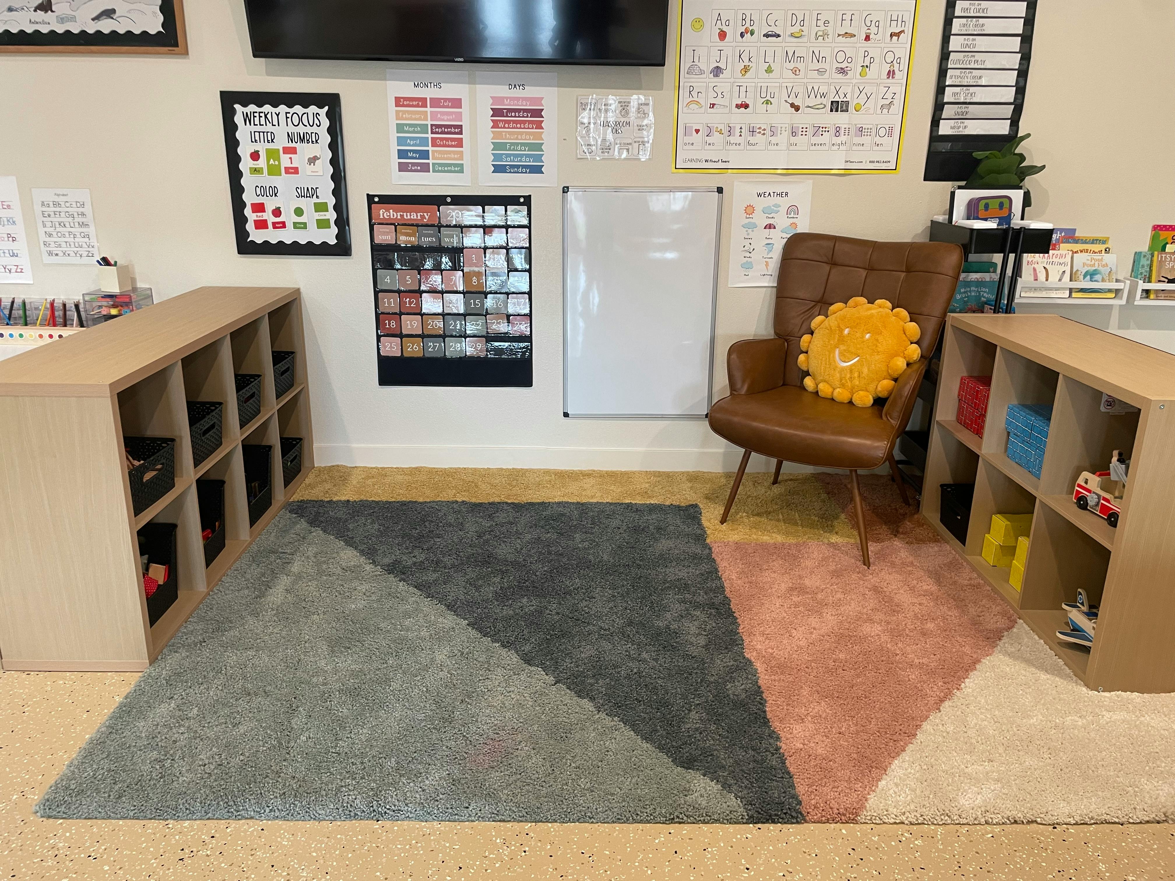 Classroom with a geometric rug, shelves, and a brown armchair