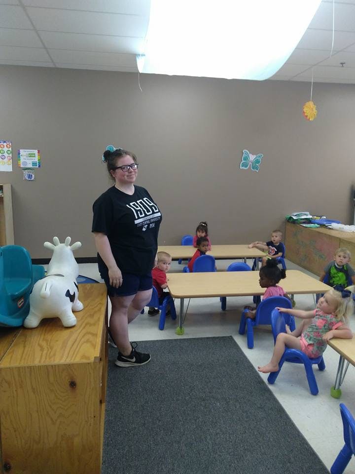 Person standing in a classroom with children seated at tables