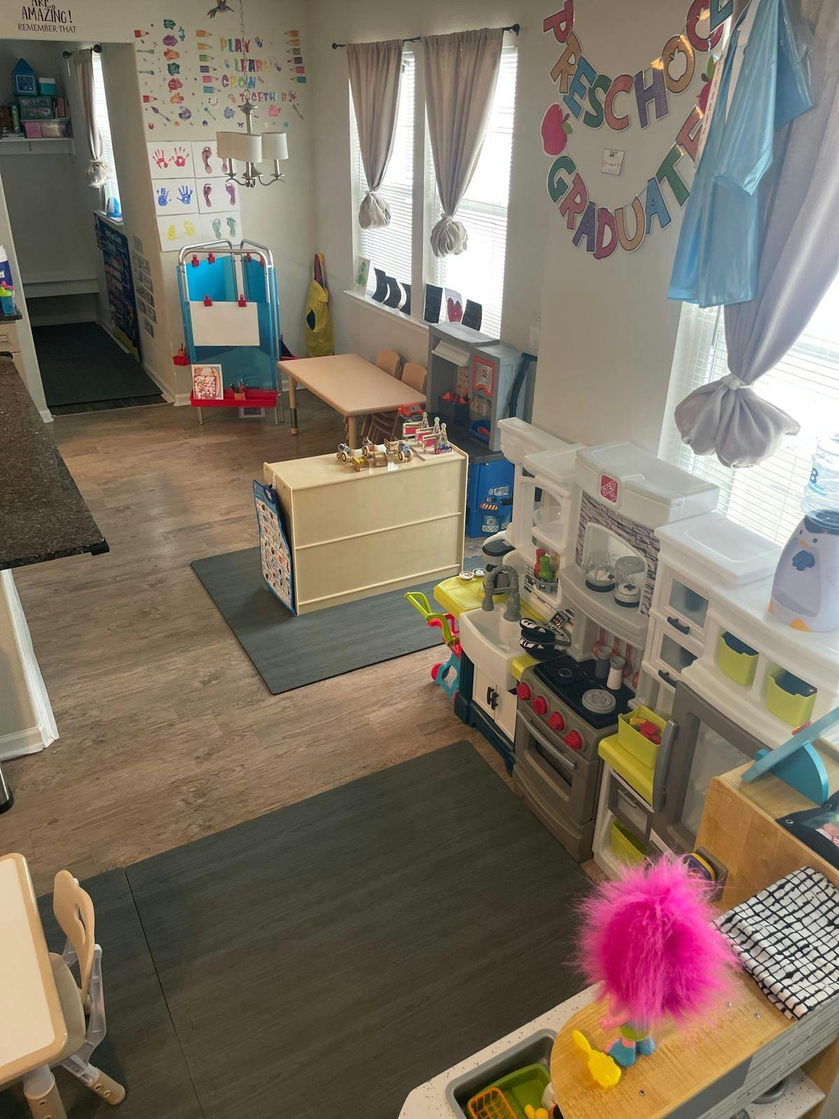 Preschool classroom with play kitchen, small tables, and a banner that says "Preschool Graduate"