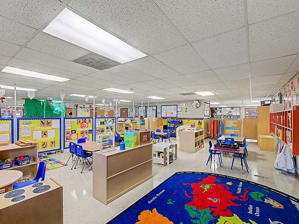 Empty classroom with small tables and chairs, and a world map rug