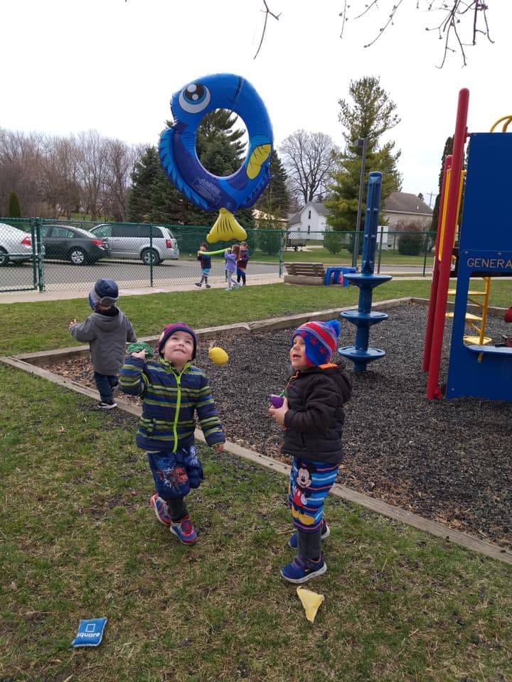 Children playing with a large blue fish balloon on a playground