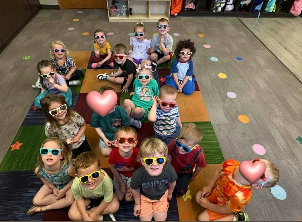 Group of children wearing sunglasses sitting on a colorful floor