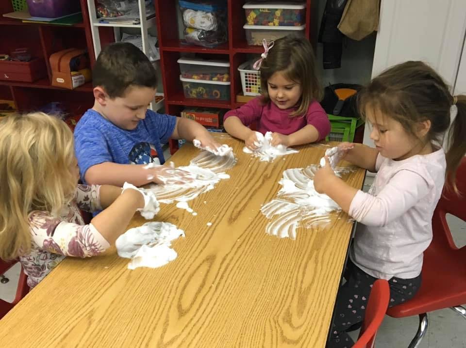 Four children playing with shaving cream at a table