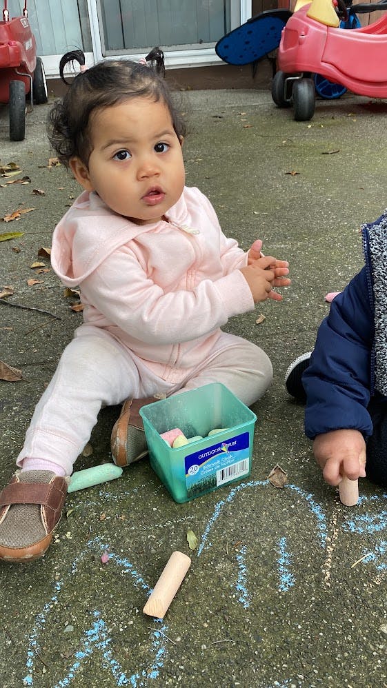 Child sitting on ground with chalk and container of box of chalk