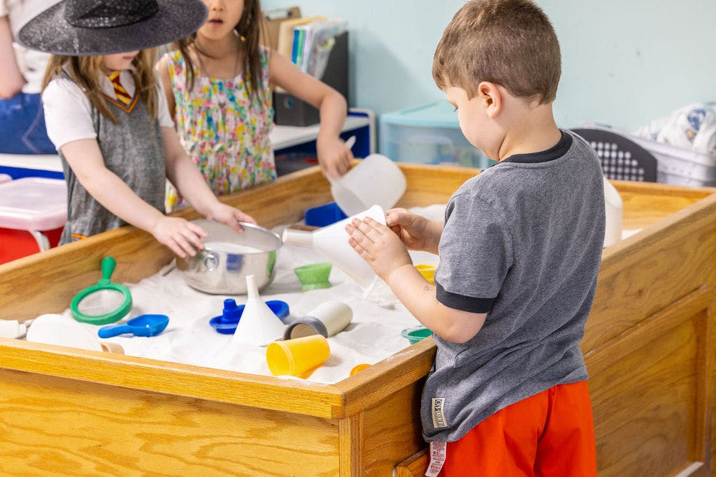 Three children playing with sand and toys in a wooden sand table