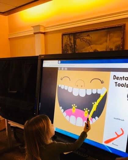 Child interacting with a large screen displaying a cartoon mouth and toothbrush