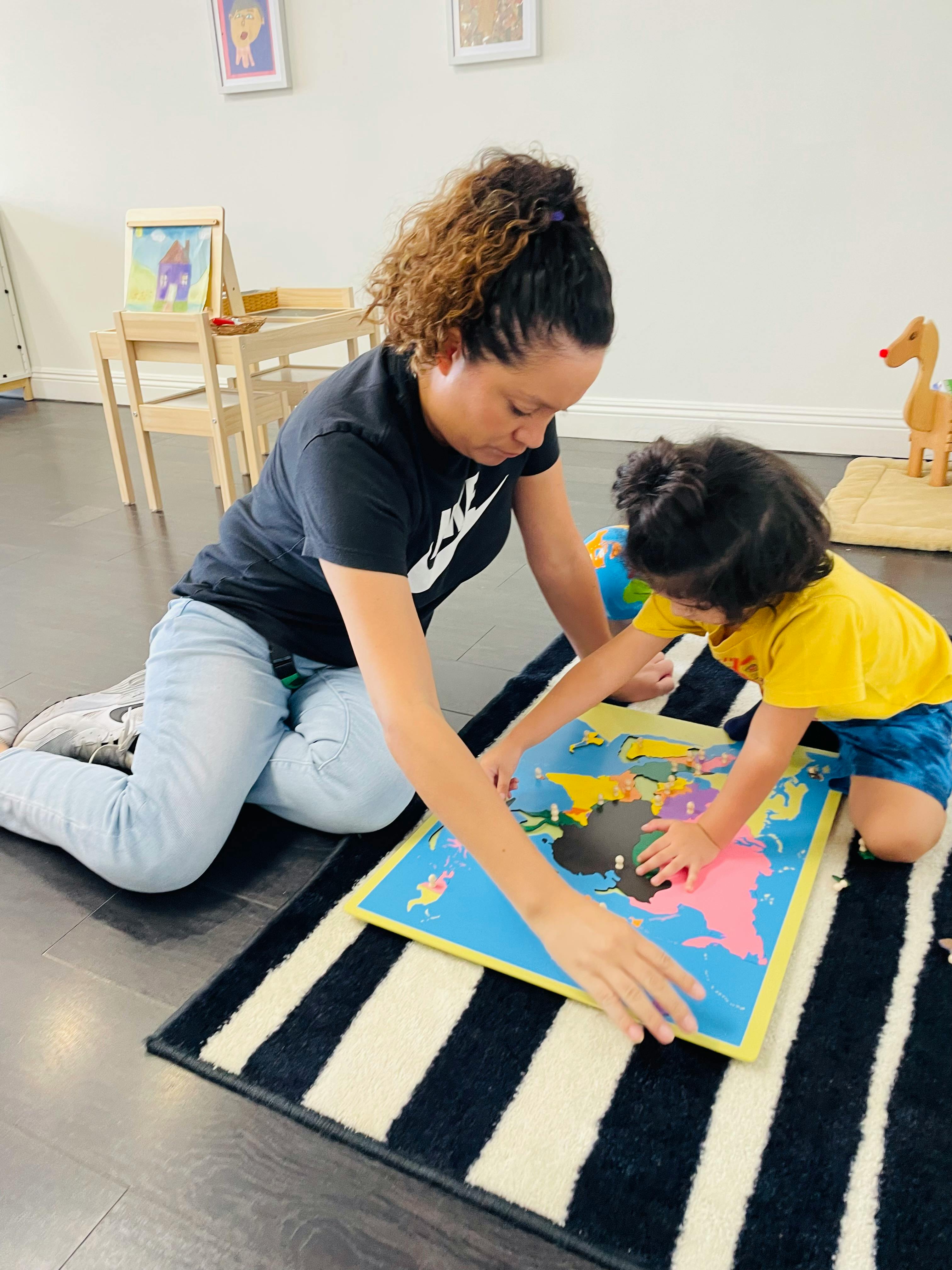 Person and child on floor playing with a world map puzzle
